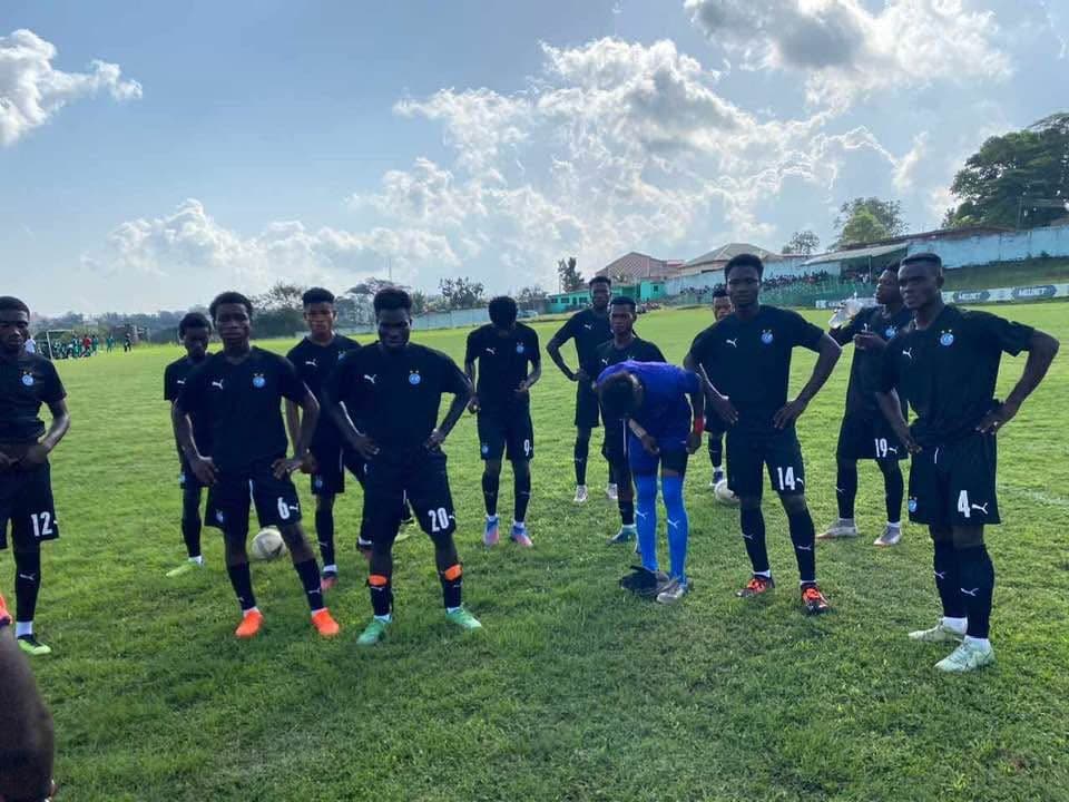 Manuel Soccer Link Academy players in black kit standing in a line on a grass pitch before a match